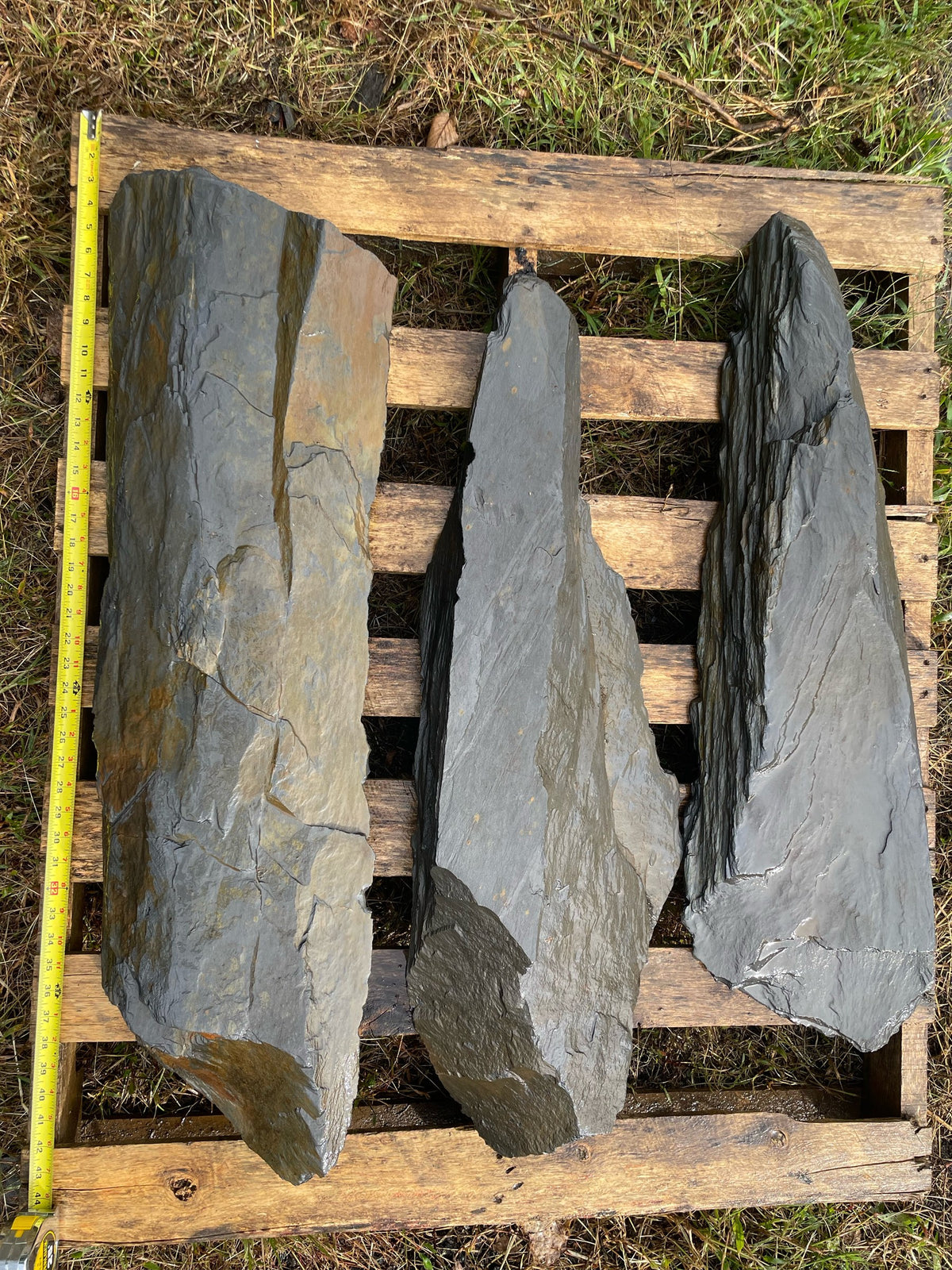 Three hand-split dark slate slabs on a pallet with tape measure