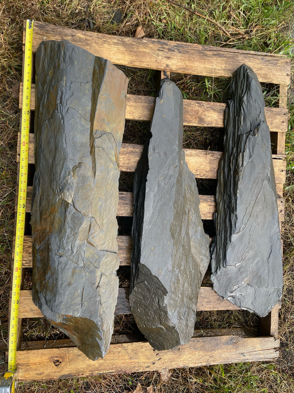 Three large dark Maryland slate slabs on a pallet, tape measure for scale