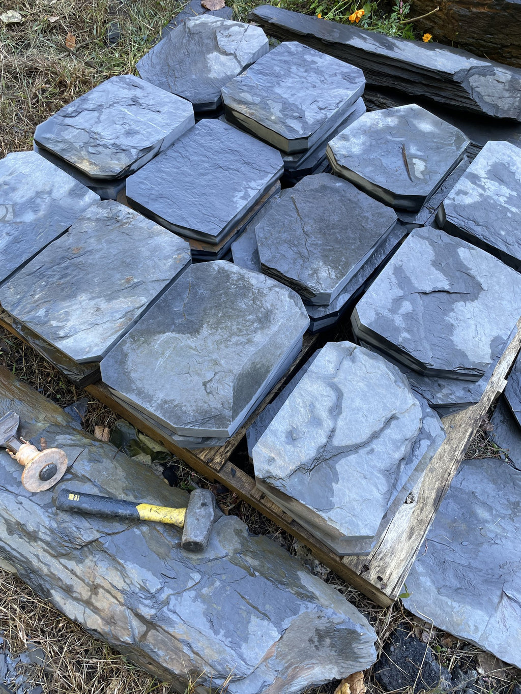 Pallet of hand-split slate steppingstones with hammer and chisel on a large slate slab